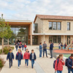 Enfants marchant devant la nouvelle école élémentaire moderne de Jacou avec une aire de jeux et des espaces végétalisés.