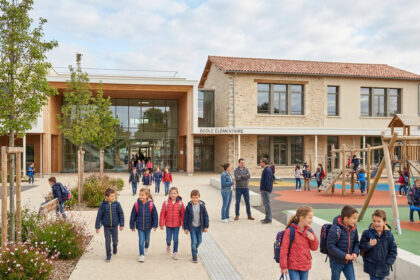 Enfants marchant devant la nouvelle école élémentaire moderne de Jacou avec une aire de jeux et des espaces végétalisés.