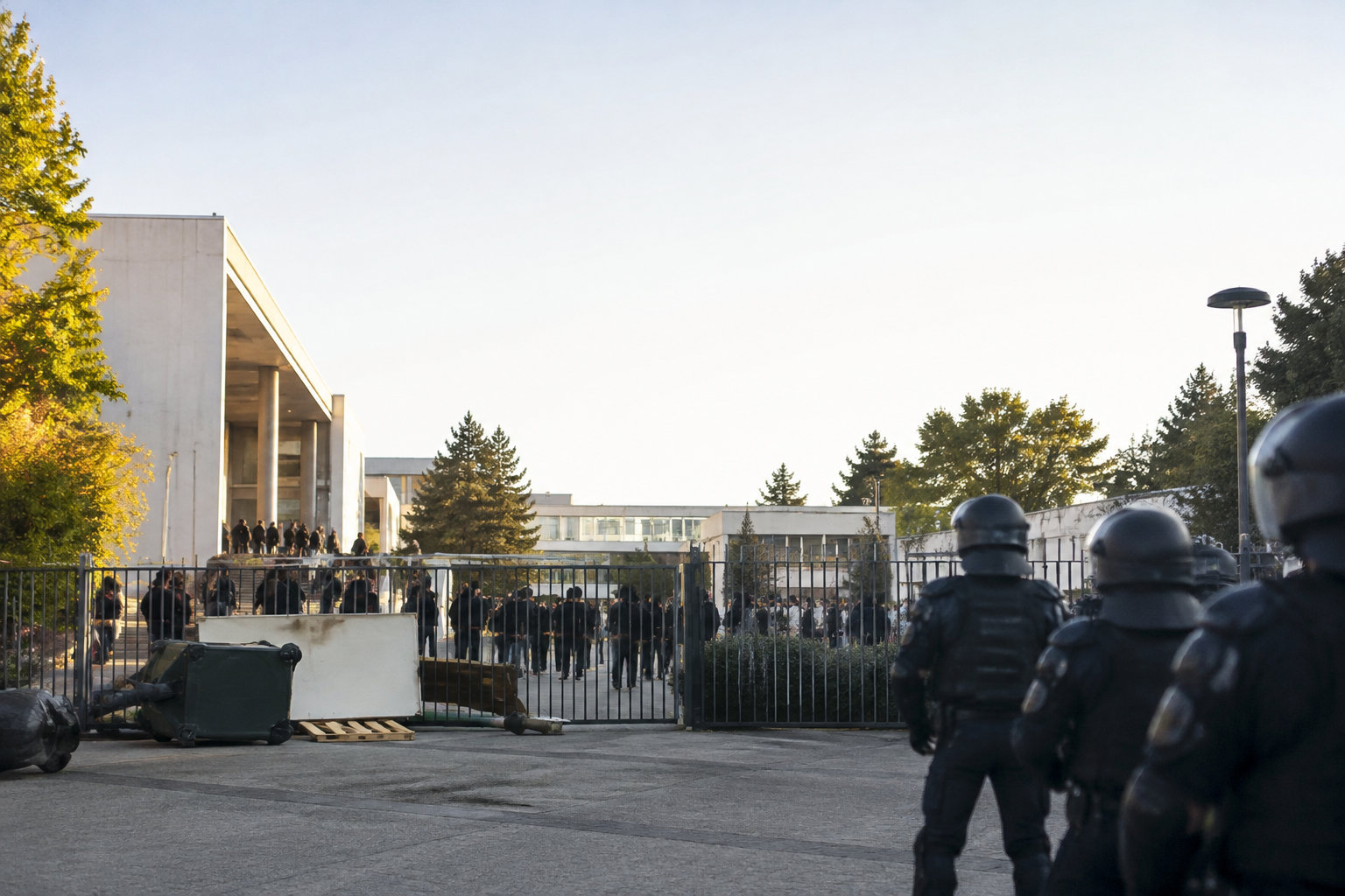 Des policiers en tenue anti-émeute font face à un groupe d'étudiants derrière une grille à l'université de Montpellier.