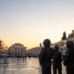 Des policiers en tenue anti-émeute sur la place de la Comédie à Montpellier au crépuscule.
